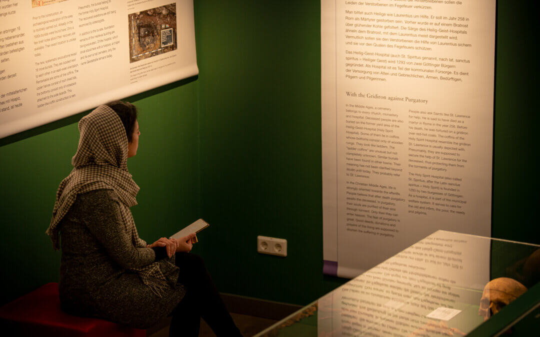 Eine Frau sitz auf einem Hocker und liest einen Text, der an der Wand hängt.